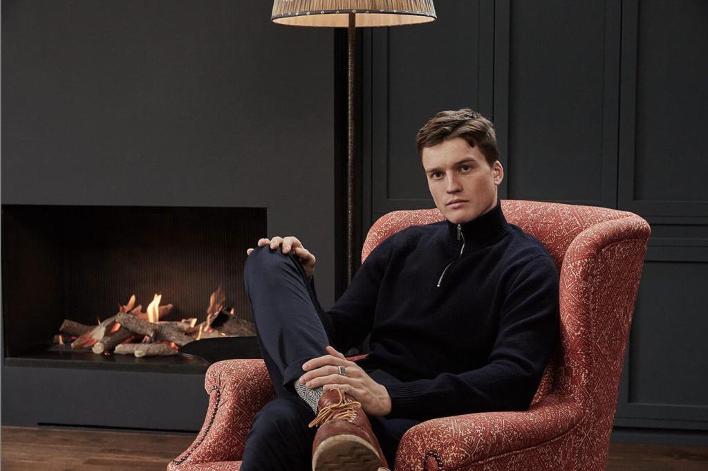 Photo of a model wearing a sweatshirt in an armchair by a fireplace in the living room.